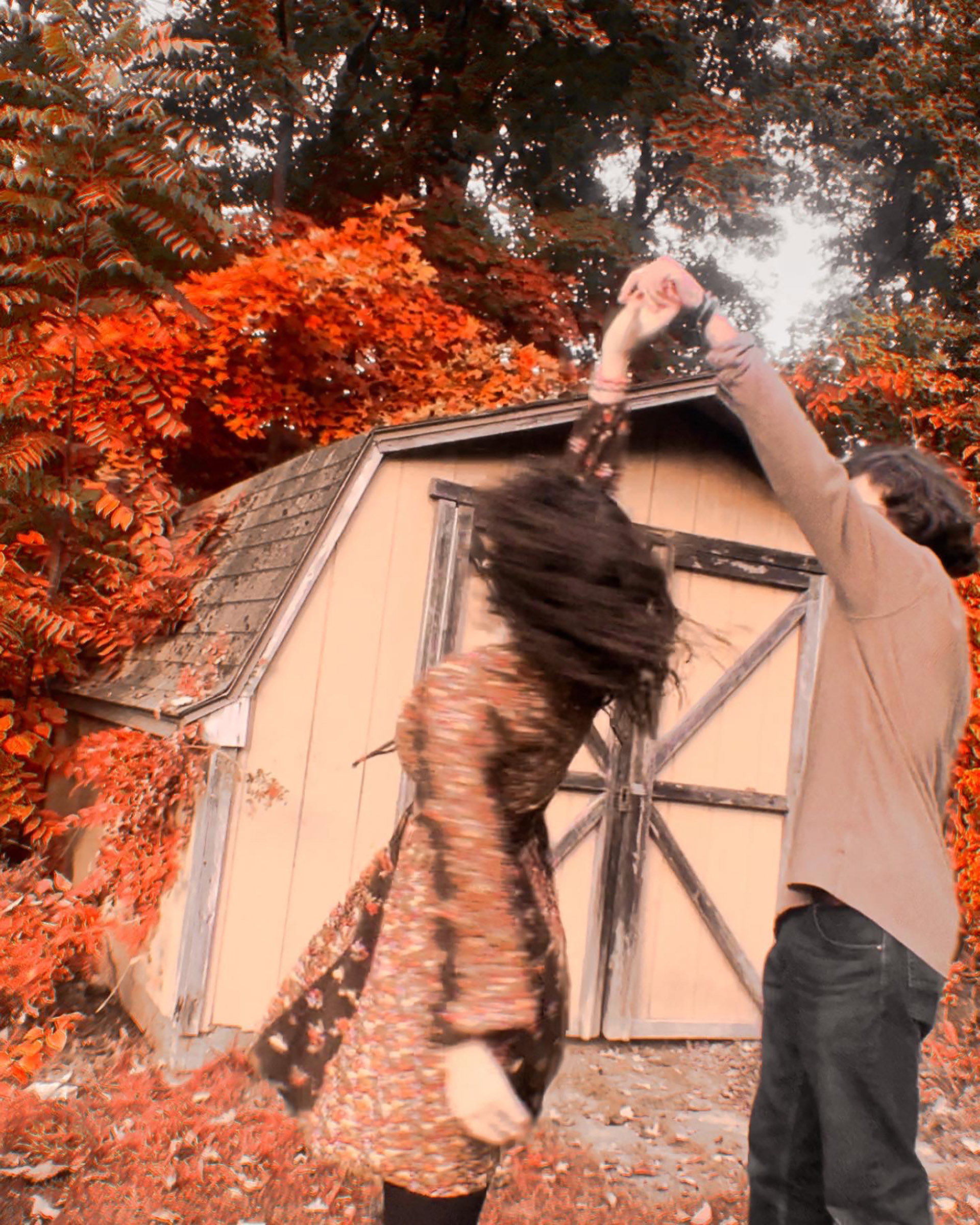 Photo of two people dancing in front of a beige shed with orange foliage 