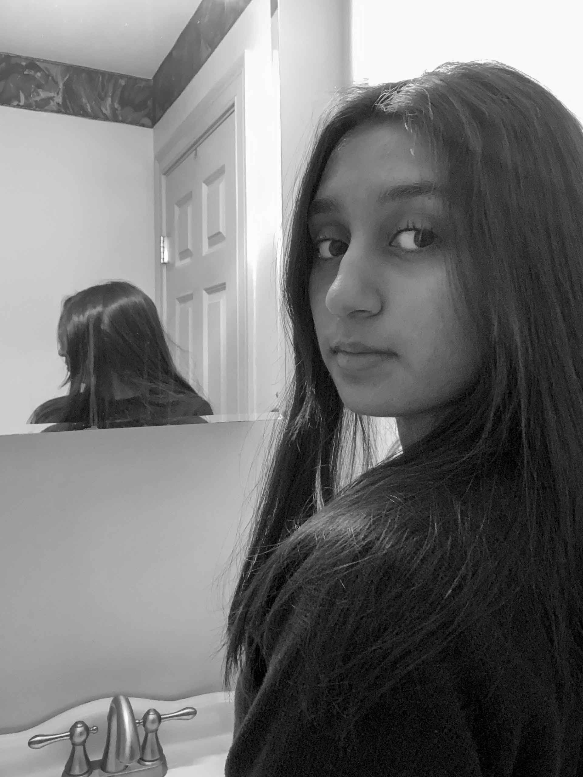 young woman in front of a mirror with the reflection of the back of her head behind her